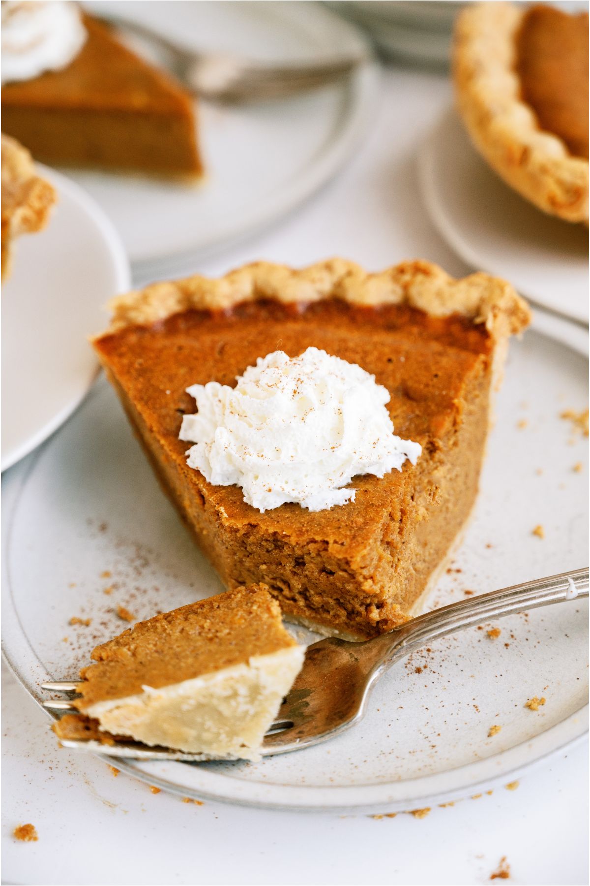 A slice of Easy Pumpkin Pie topped with whip cream on a plate with a fork that has sliced a bite out of it.