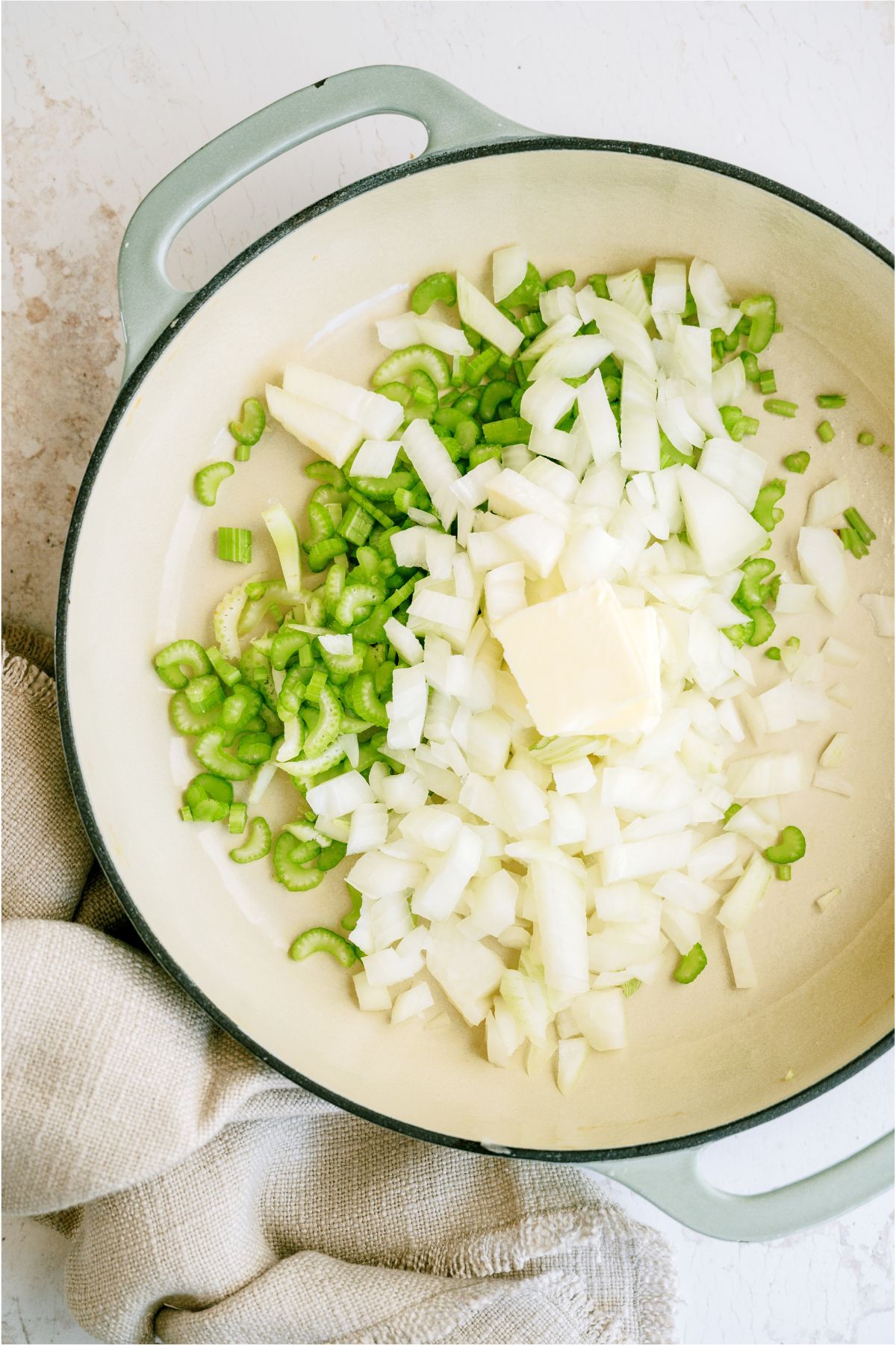 A skillet with diced celery and onion with a pat of butter on top.