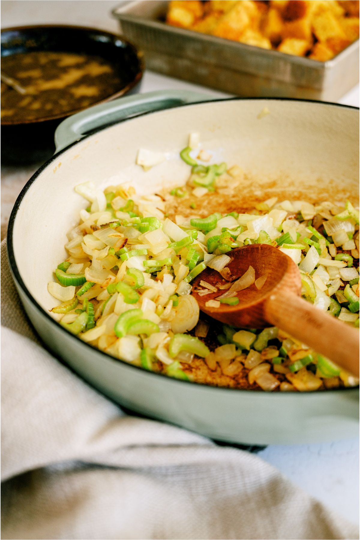 Sauteing onions and celery in a skillet with a wooden spoon.