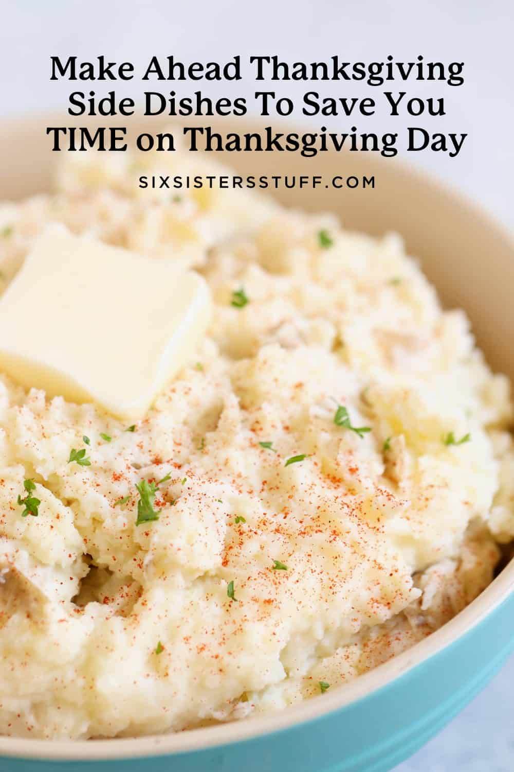 A bowl of mashed potatoes topped with a pat of butter and sprinkled with herbs and seasoning. 