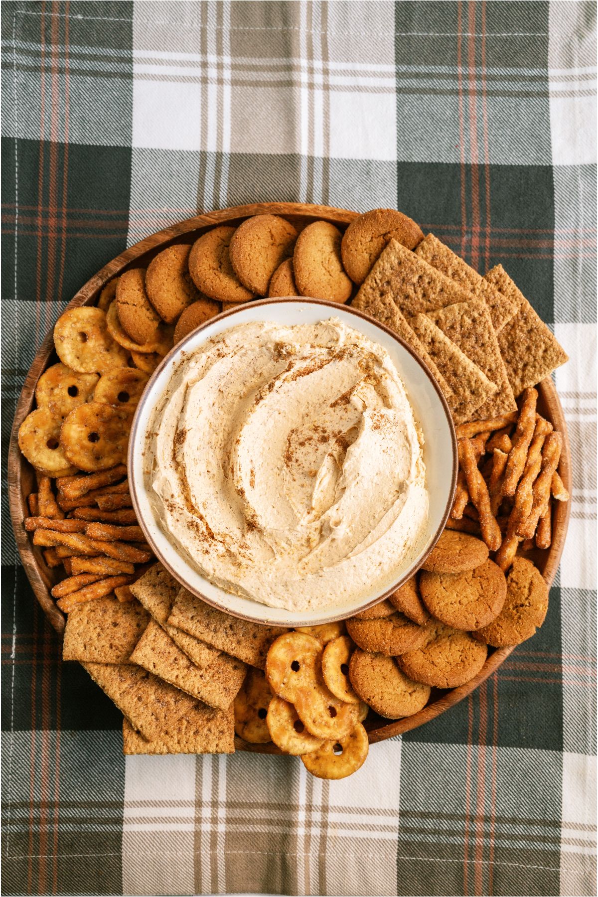 Pumpkin Dip in a bowl surrounded by cookies and crackers on a serving tray with a plaid tablecloth underneath.