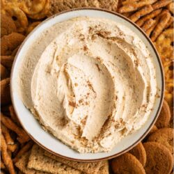 A serving bowl filled with Pumpkin Dip surrounded by cookies and crackers on a serving tray.