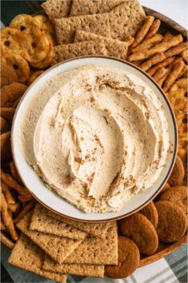 A serving bowl filled with Pumpkin Dip surrounded by cookies and crackers on a serving tray.