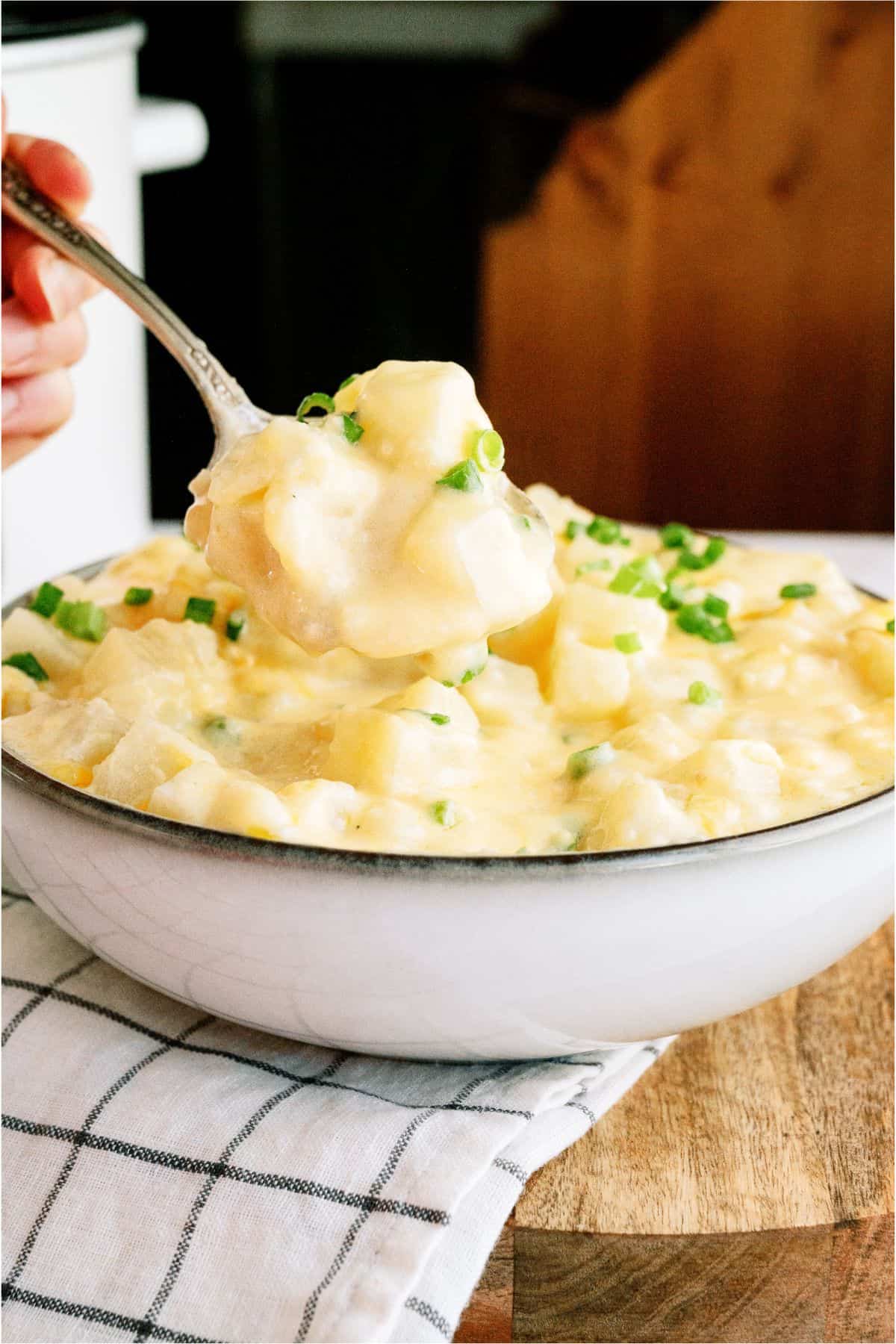 A spoon lifting a serving of Slow Cooker Cheesy Potatoes out of a bowl