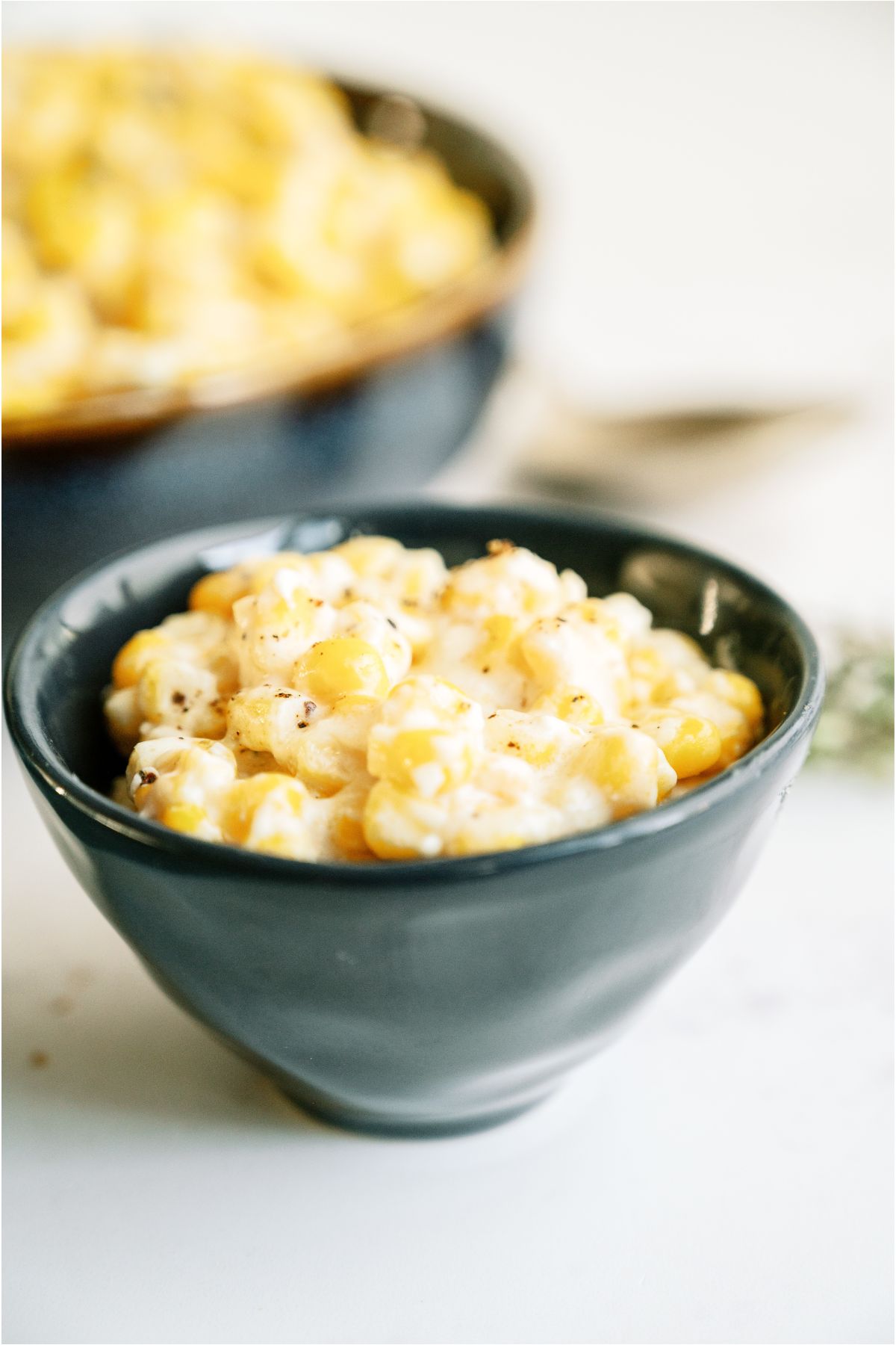 Slow Cooker Creamed Corn in a small bowl with a larger serving bowl full of Slow Cooker Creamed Corn in the backgroud.