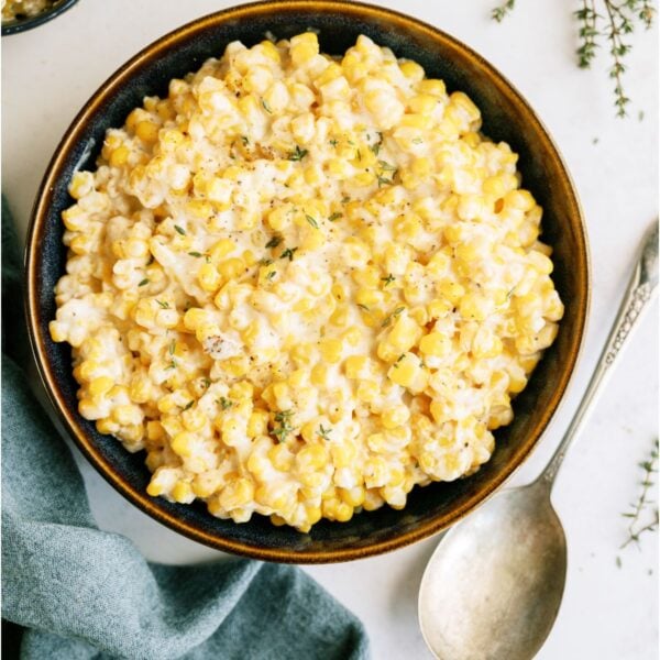 Slow Cooker Creamed Corn in a serving bowl with a serving spoon on the side.