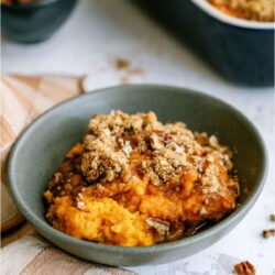 A blue bowl with a serving of Sweet Potato Casserole in it, with the remaining casserole in the background.