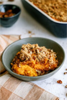 A blue bowl with a serving of Sweet Potato Casserole in it, with the remaining casserole in the background.