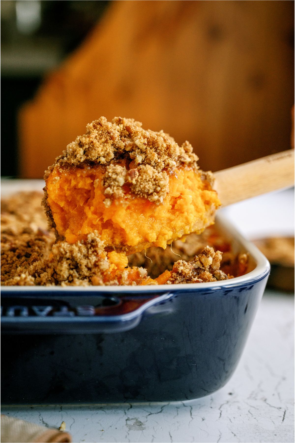 A wooden spoon lifting a scoop of Sweet Potato Casserole out of the casserole dish.