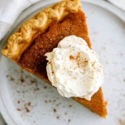 A slice of sweet potato pie topped with whipped cream and a sprinkle of cinnamon, served on a white plate.