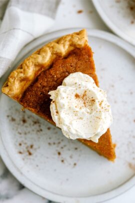 A slice of sweet potato pie topped with whipped cream and a sprinkle of cinnamon, served on a white plate.