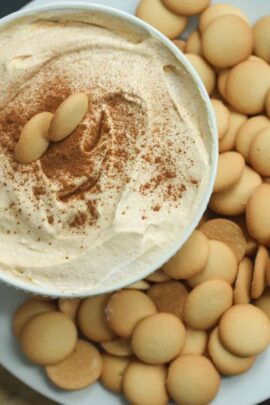 A bowl of creamy pumpkin dip sprinkled with cinnamon, surrounded by vanilla wafer cookies.