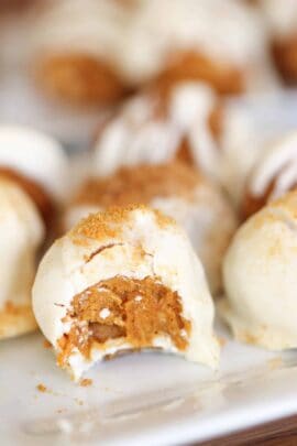 A close-up of white chocolate-covered pumpkin spice truffles, with a visible bite revealing a crumbly, orange-brown center.