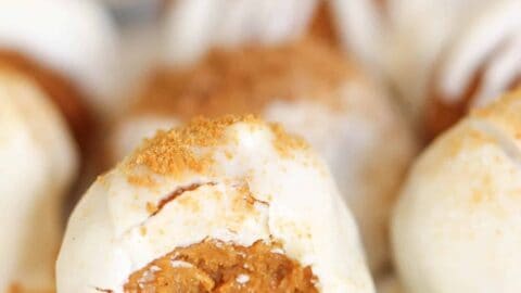 A close-up of white chocolate-covered pumpkin spice truffles, with a visible bite revealing a crumbly, orange-brown center.