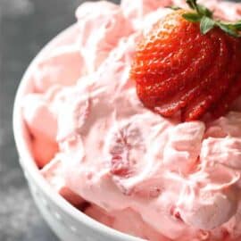 A white bowl filled with strawberry fluff salad, topped with a sliced strawberry.