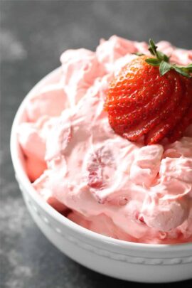 A white bowl filled with strawberry fluff salad, topped with a sliced strawberry.