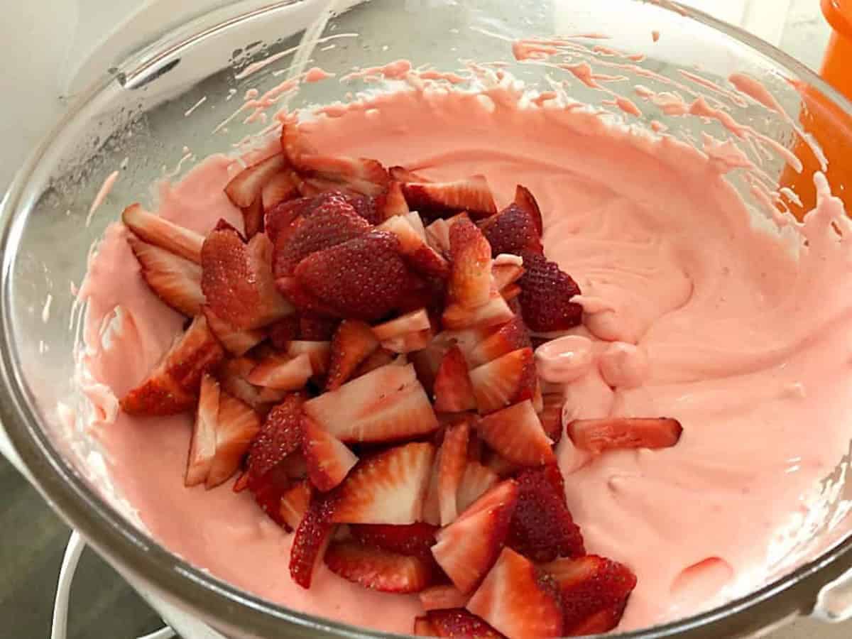 A glass bowl filled with pink strawberry mousse topped with sliced fresh strawberries.