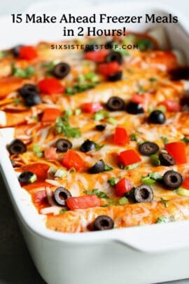Close-up of a white casserole dish filled with enchiladas topped with melted cheese, diced tomatoes, black olives, and green onions.
