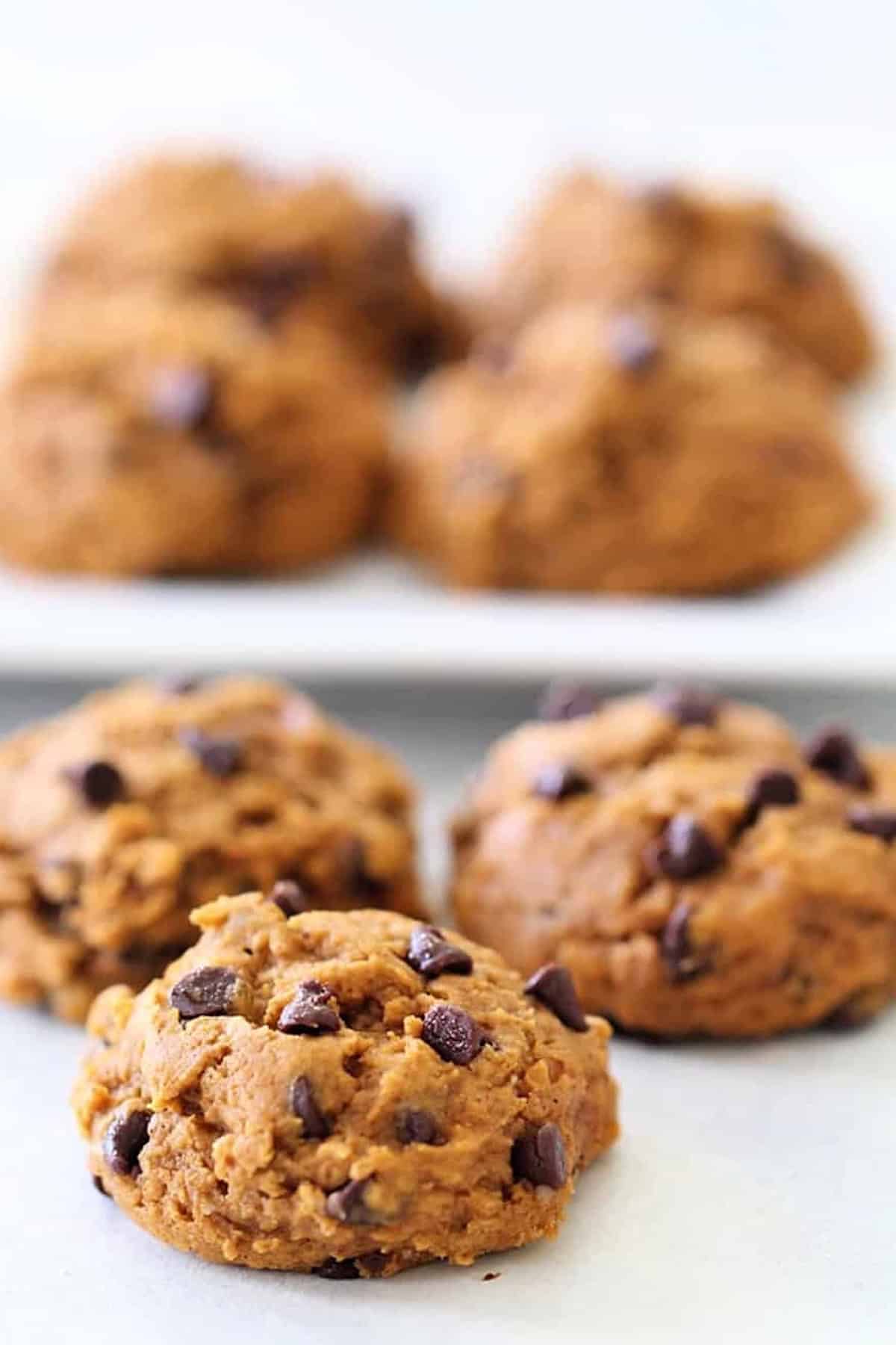 Close-up of freshly baked chocolate chip cookies on a surface, with more cookies blurred in the background.