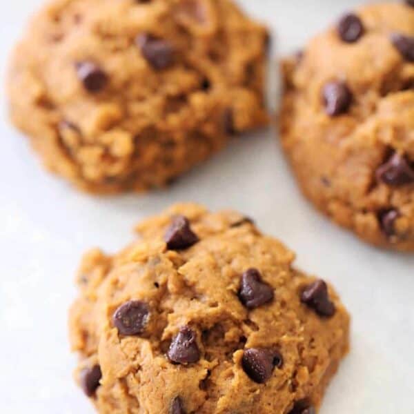 Three chocolate chip cookies on a white surface. They have a light brown color with visible chocolate chips.