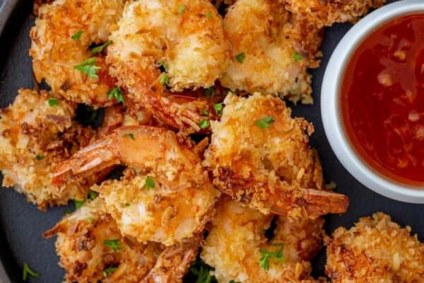 A plate of crispy, golden-brown shrimp with a side of red dipping sauce, garnished with parsley.