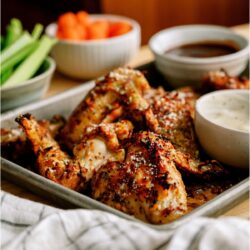 A pan of Air Fryer Garlic Parmesan Chicken Wings with two sauces on the side and chopped celery and carrots in the background.