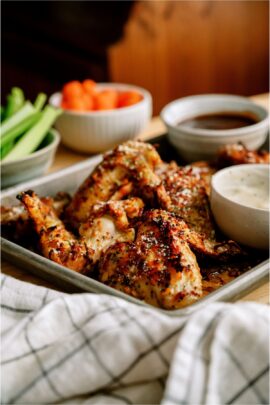 A pan of Air Fryer Garlic Parmesan Chicken Wings with two sauces on the side and chopped celery and carrots in the background.