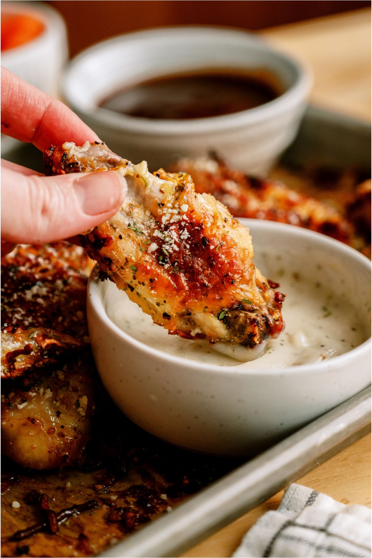 A hand dipping a Air Fryer Garlic Parmesan Chicken Wing in a cup of ranch with the remaining wings in the background.