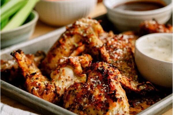 A pan of Air Fryer Garlic Parmesan Chicken Wings with two sauces on the side and chopped celery and carrots in the background.