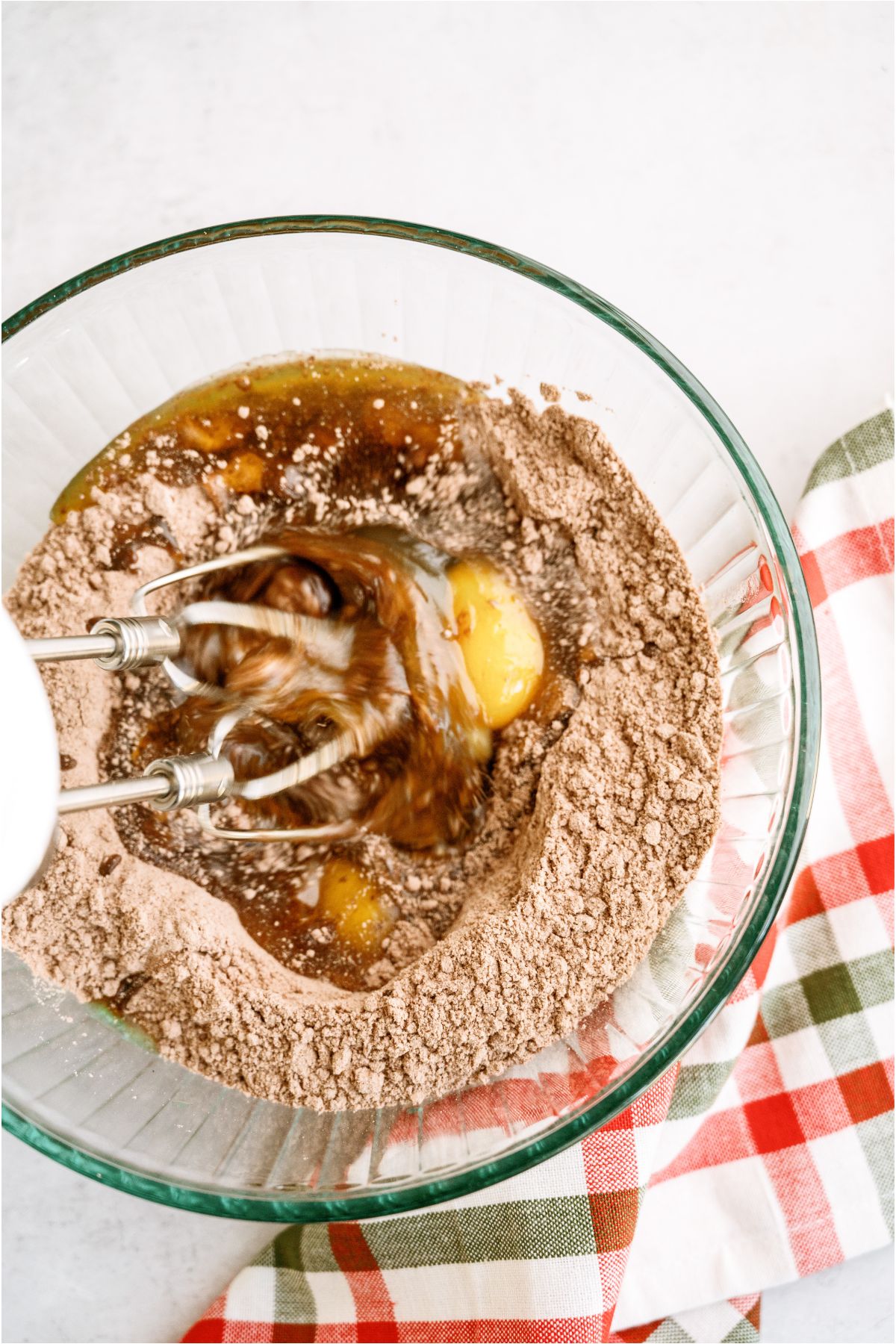 Cake mix in a glass mixing bowl with eggs and oil being mixed with a hand mixer.