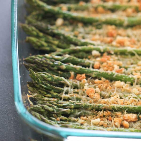 Glass dish containing roasted asparagus spears topped with breadcrumbs and grated cheese.