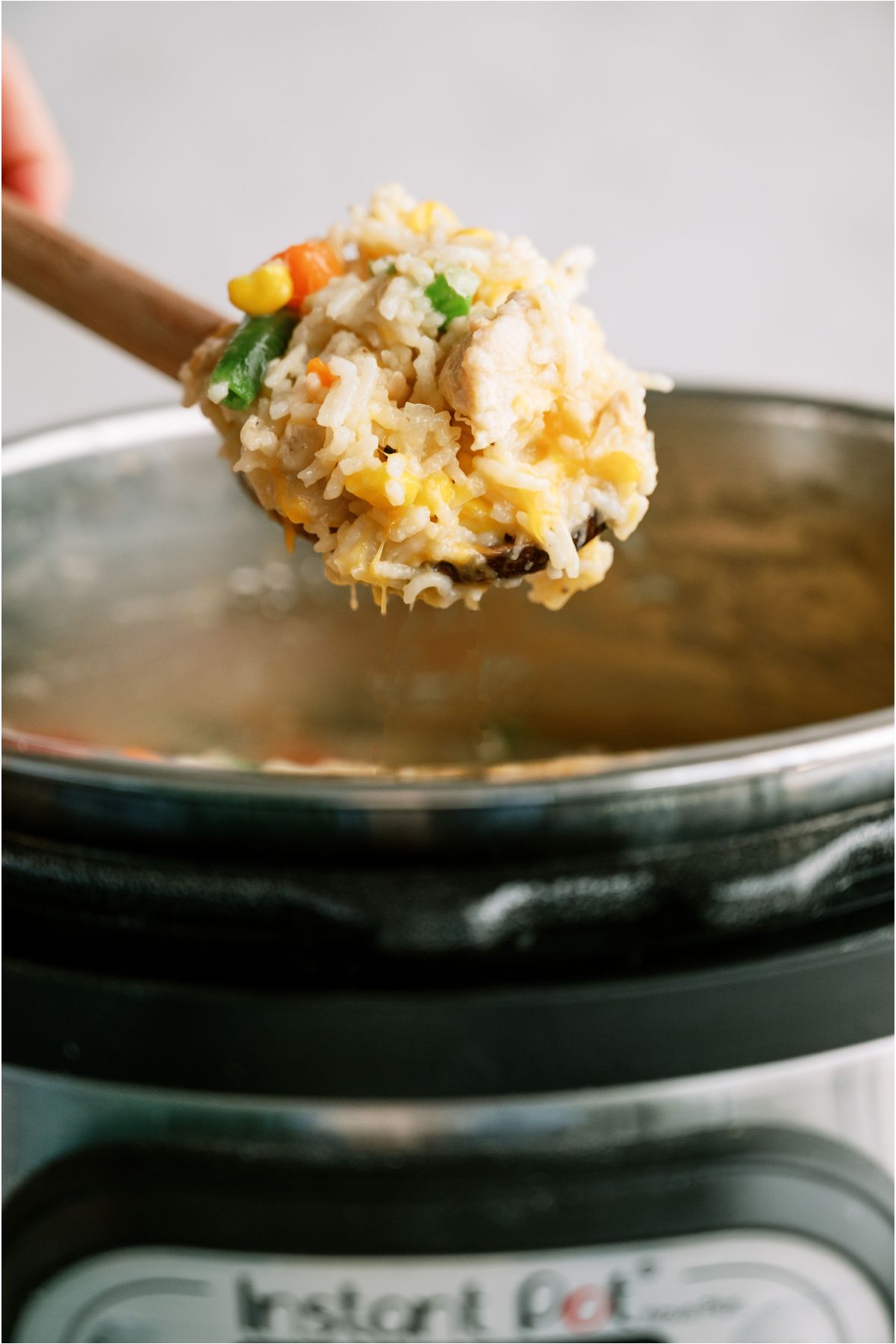 A wooden spoon lifitng out a scoop of Instant Pot Cheesy Chicken and Rice out of the Instant Pot.