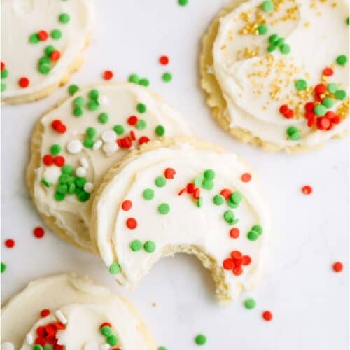 Top view of Super Soft Sugar Cookies frosted and with sprinkles. Two stacked on top of each other with the top one missing a bite.