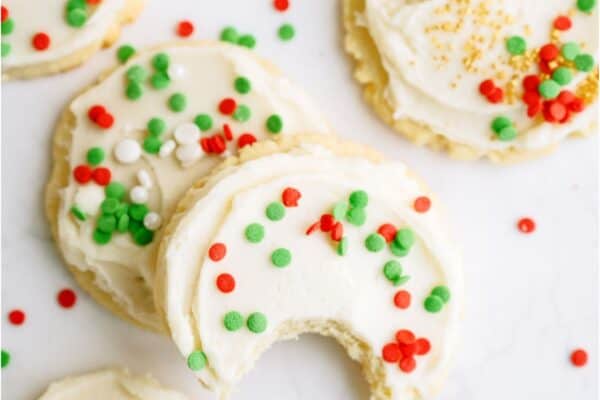 Top view of Super Soft Sugar Cookies frosted and with sprinkles. Two stacked on top of each other with the top one missing a bite.