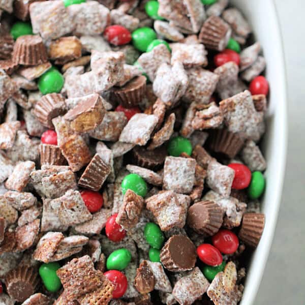 A white bowl filled with chocolate muddy buddies, mini peanut butter cups, and red and green candy-coated chocolates.
