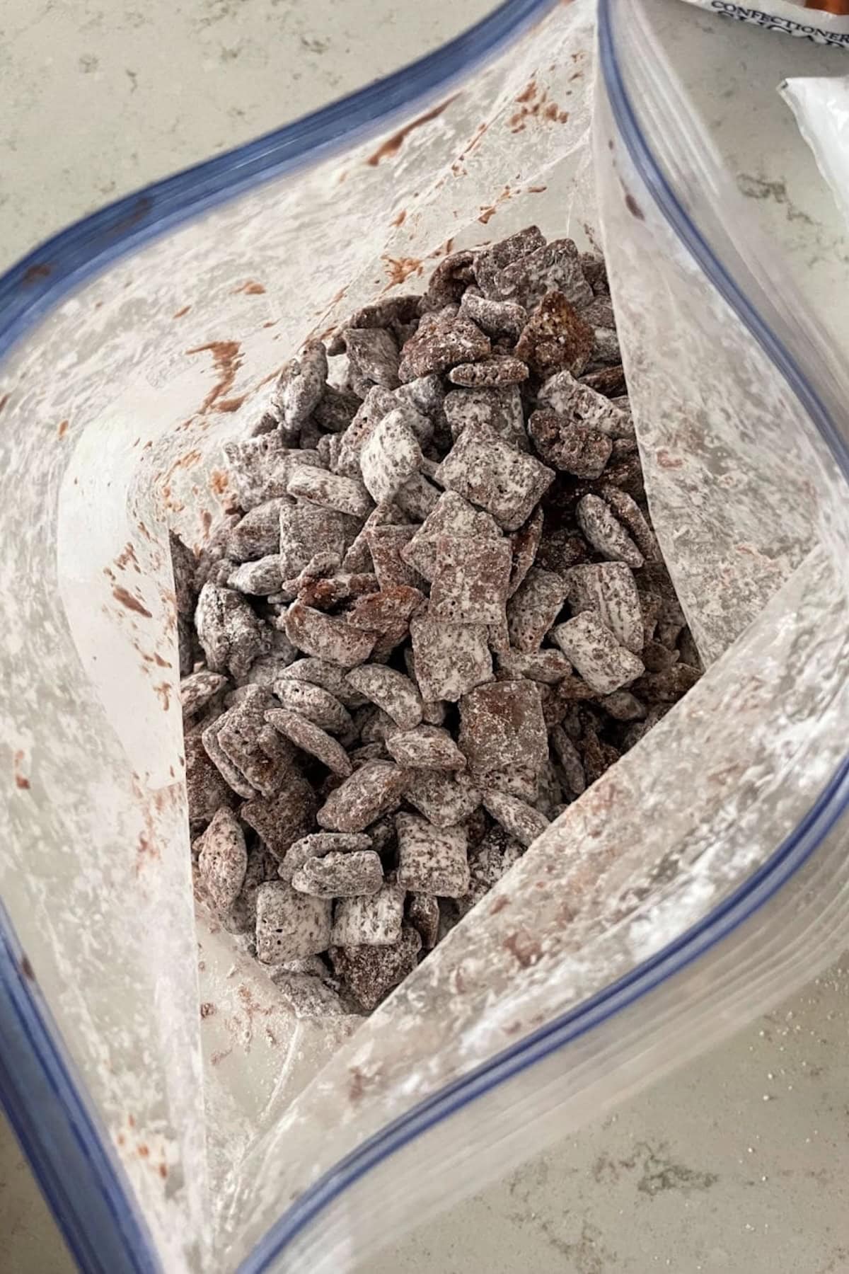 A plastic bag filled with chocolate-coated cereal pieces dusted with powdered sugar.