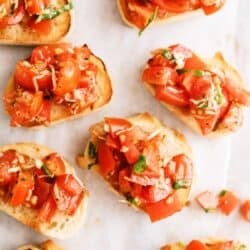 Sliced baguette topped with diced tomatoes, basil, and garlic, arranged on a white surface.