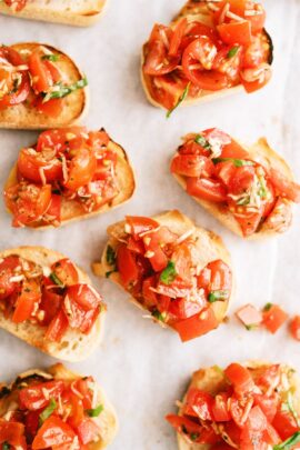 Sliced baguette topped with diced tomatoes, basil, and garlic, arranged on a white surface.