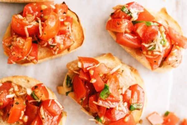 Sliced baguette topped with diced tomatoes, basil, and garlic, arranged on a white surface.