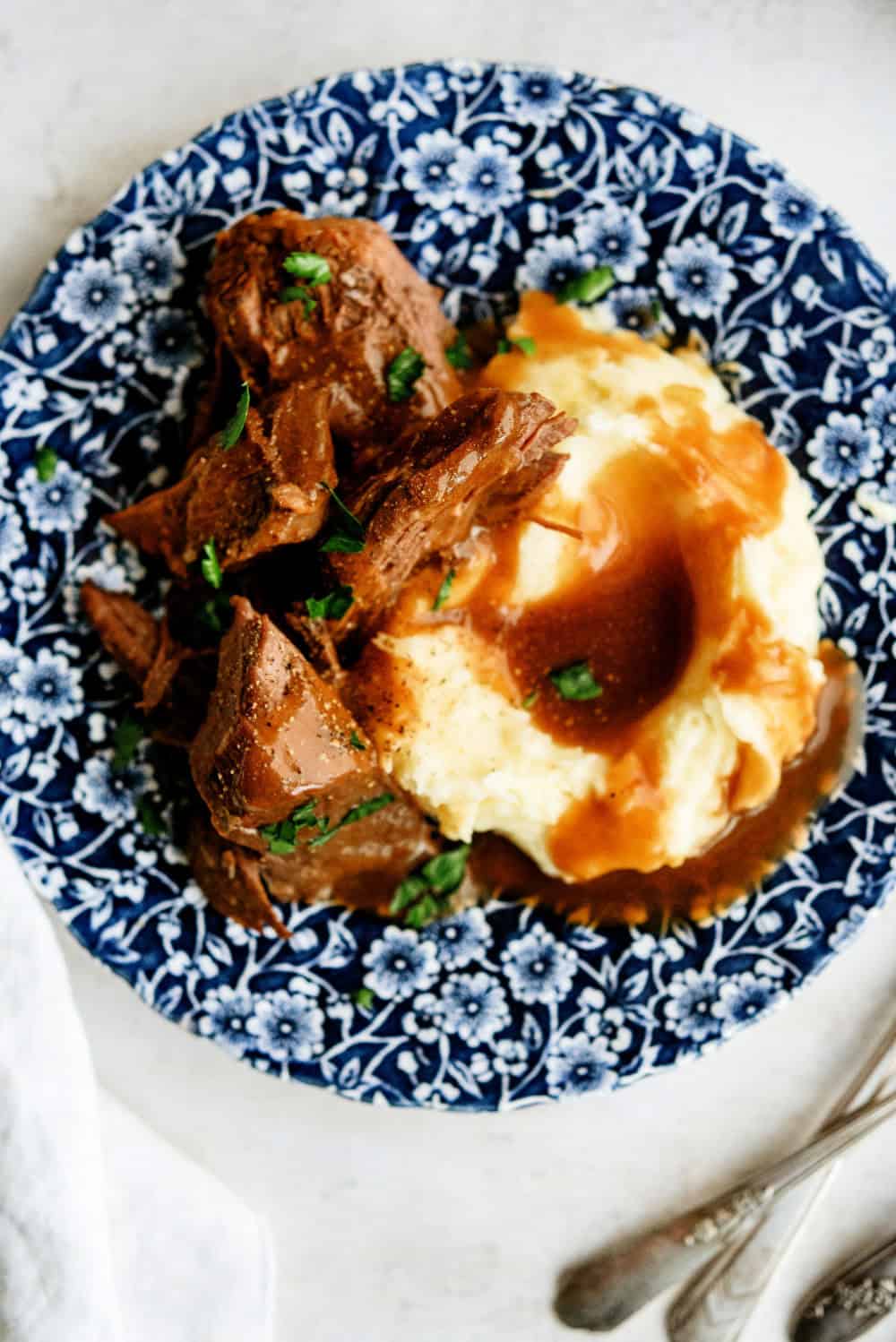 Slow Cooker Copycat Texas Roadhouse Beef Pot Roast on a plate with mashed potatoes and gravy.