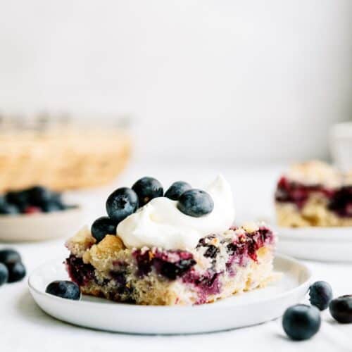 blueberry coffee cake with whipped topping and fresh blueberries on a plate