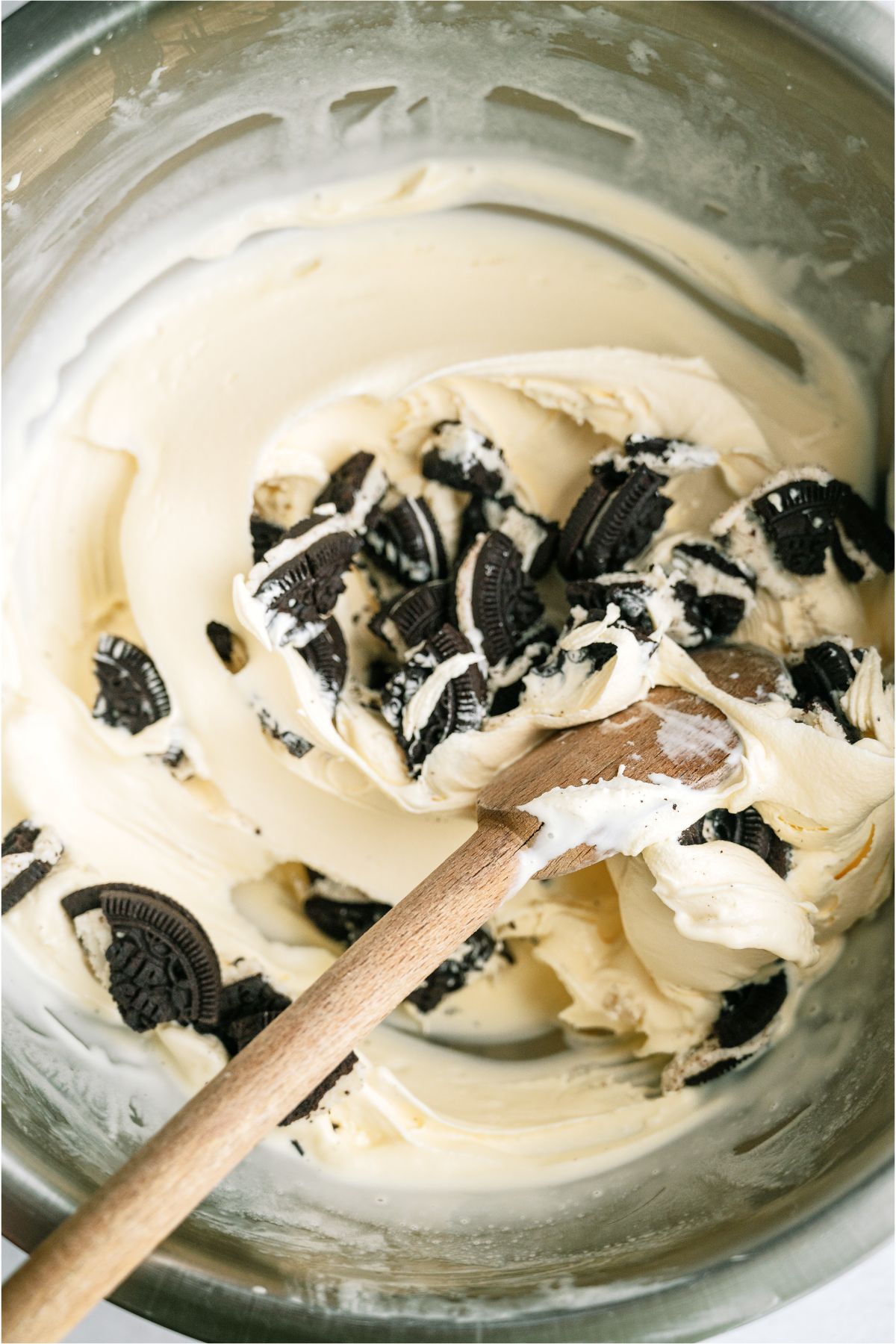 Ice cream in a bowl with a wooden spoon stirring in crushed up oreo cookies