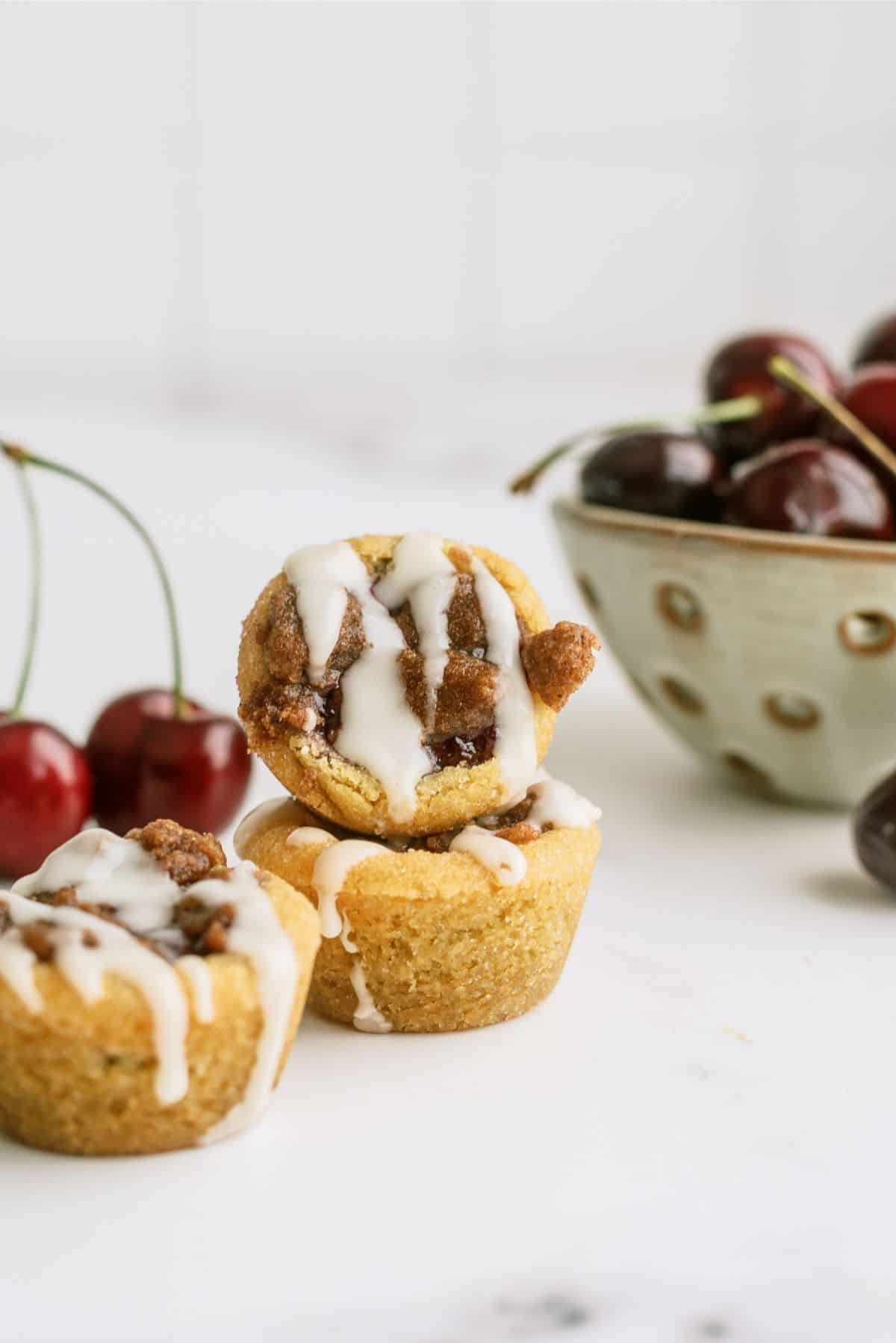 2 Cherry Cobbler Cookie Cups stacked with a bowl of cherries in the background