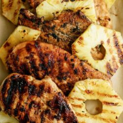 Grilled chicken breasts and pineapple rings arranged on a plate.