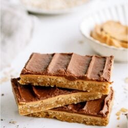 3 chocolate peanut butter bars stacked on top of each other on a white background.