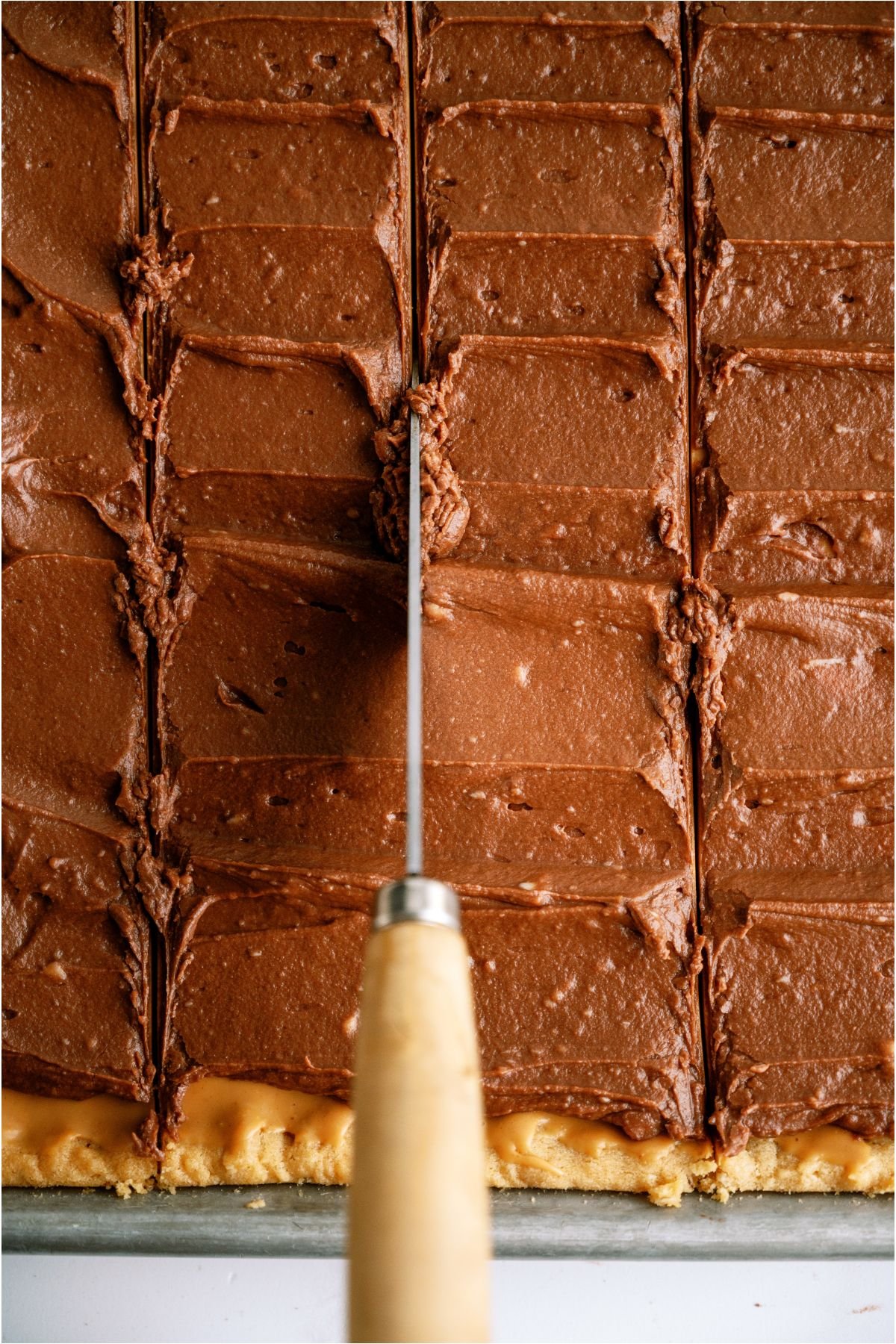 A knife cutting through a pan of chocolate covered peanut butter bars.