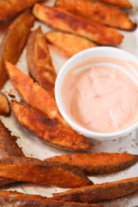 Potato wedges on a tray with a small bowl of pink dipping sauce.