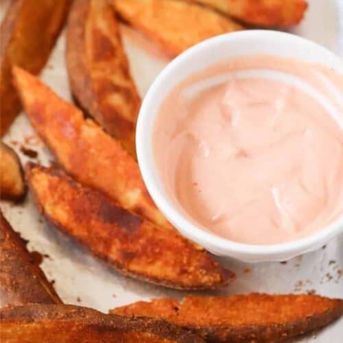 Potato wedges on a tray with a small bowl of pink dipping sauce.