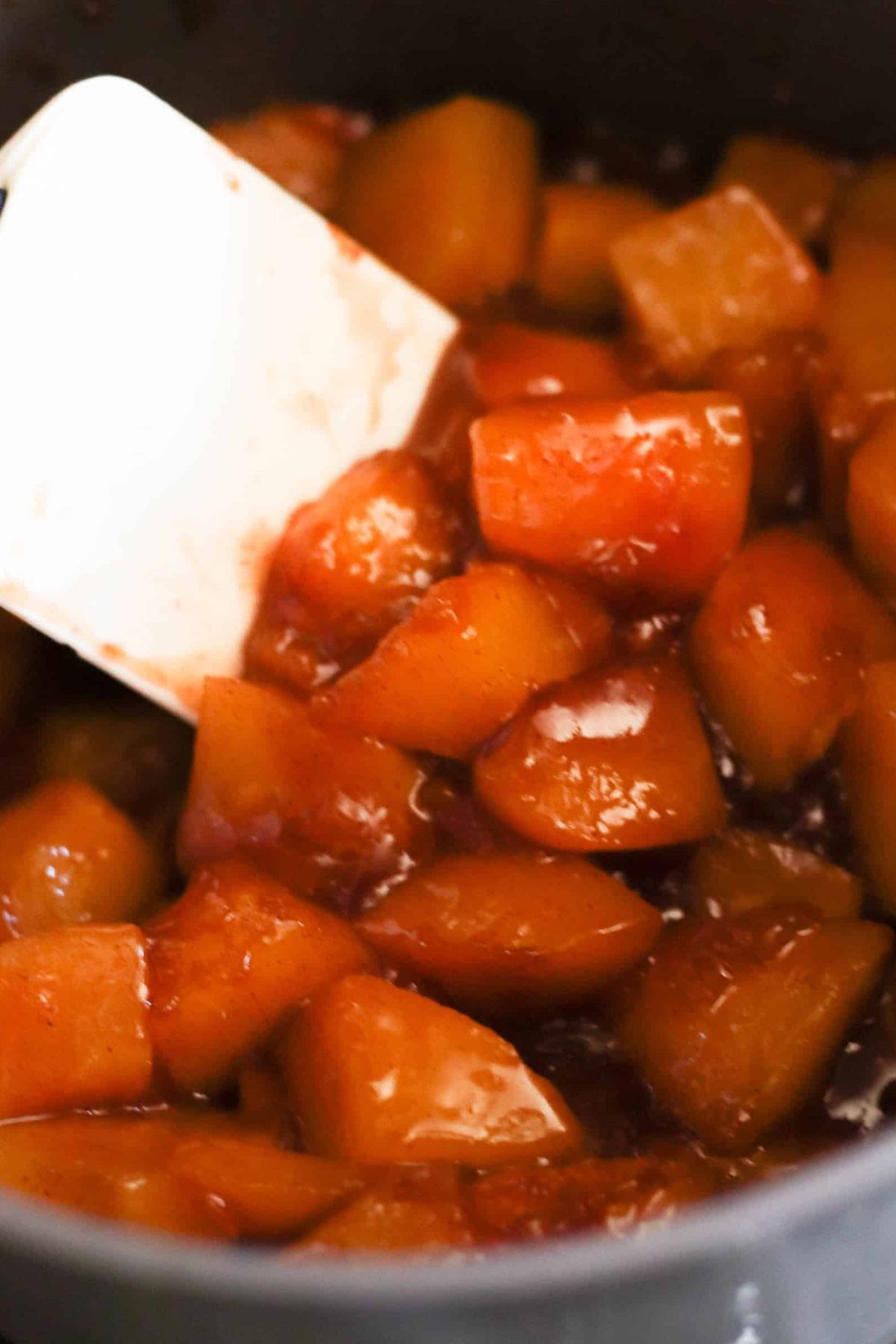 Rubber spatula stirring peach mixture in mixing bowl.