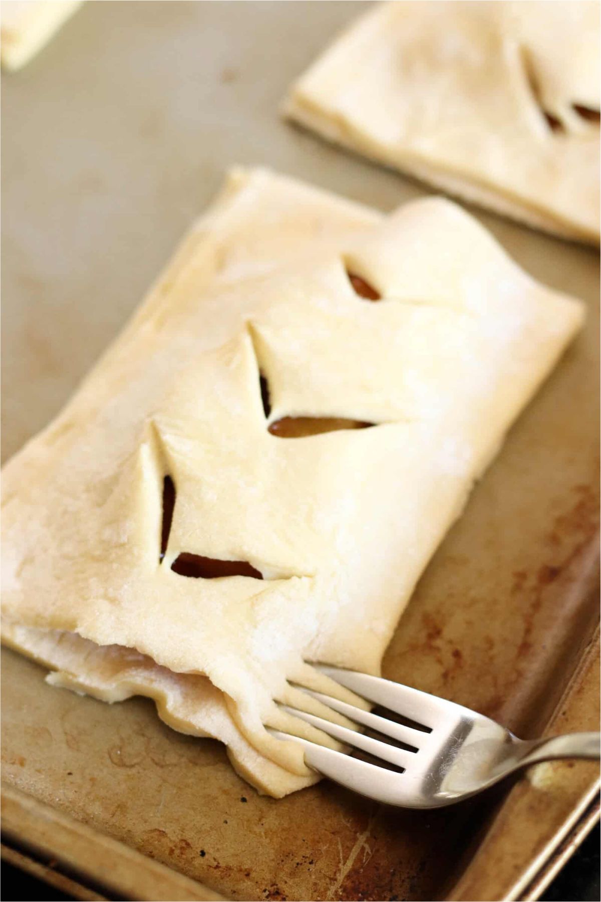 Unbaked Hand Peach Pie on baking sheet with a fork sealing the edges around the pie.